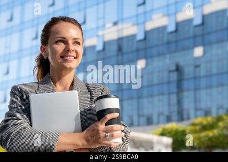 Young businesswoman holding digital tablet and coffee mug outdoors on city street Stock Photo