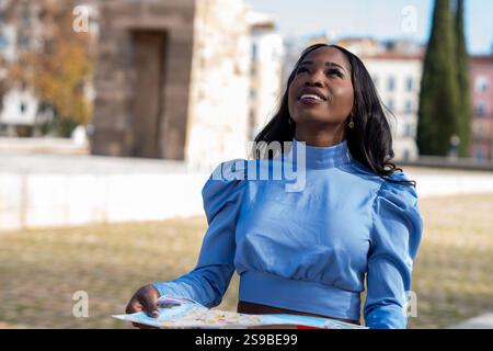 Young black female tourist holding a map and looking up while visiting a city center Stock Photo