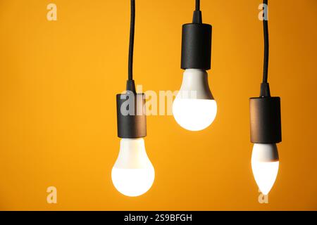 Light bulbs hanging on cords against orange background, space for text Stock Photo