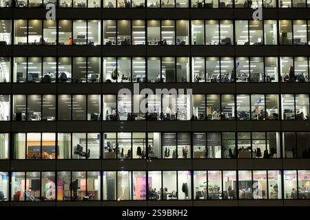 People workers working inside office buildings offices windows lit up at night nighttime riverside modern glass building London England UK Britain Stock Photo