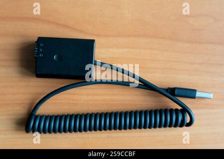 A black coiled USB cable is placed on a wooden surface. The connector is visible at one end, showcasing its design and functionality. The setting is s Stock Photo