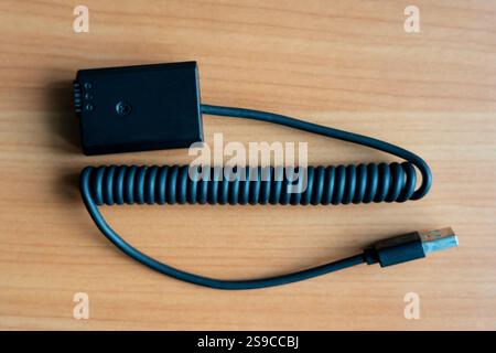 A coiled USB cable connector rests on a wooden surface. It features a rectangular black connector at one end and a standard USB attachment at the othe Stock Photo