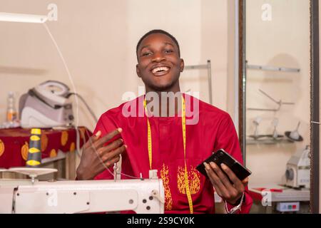 An African tailor using his phone while working in his workshop. Stock Photo