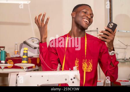 An African tailor using his phone while working in his workshop. Stock Photo