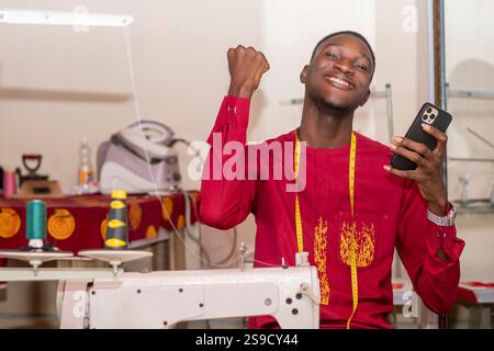 An African tailor using his phone while working in his workshop. Stock Photo