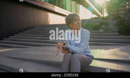 Full length shot Caucasian older mature retired woman female pensive businesswoman using mobile phone in city with data connections business Stock Photo