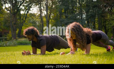 Healthy practice sport strong multiracial couple Arabian Indian man fitness trainer training with Caucasian woman pair workout in nature park doing Stock Photo