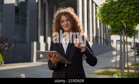 Caucasian elegant business woman using digital tablet outside happy businesswoman executive holding pad device on city street showing thumb up gesture Stock Photo