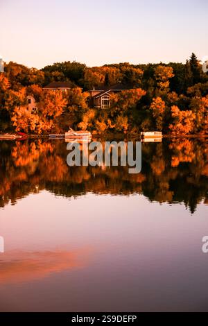 A lake with a house in the background and a few boats floating on the water. The water is calm and the sky is orange Stock Photo