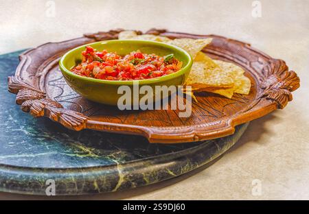 Fresh organic salsa in a vintage bowl and corn chips on an antique wooden plate on a marble tray. Stock Photo