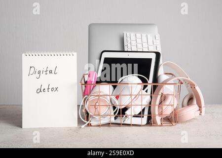 Notebook with text DIGITAL DETOX and basket full of modern gadgets on light background Stock Photo