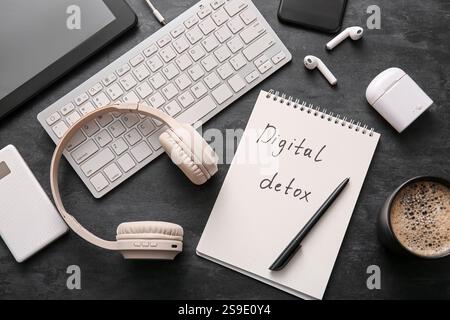Notebook with text DIGITAL DETOX, cup of coffee and different gadgets on dark background Stock Photo