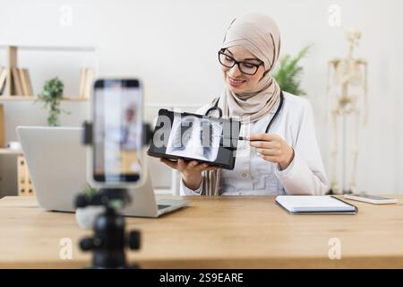 Middle Eastern female doctor records online lesson on lung X-ray diagnosis. Educating audience on respiratory health using digital tools. Stock Photo