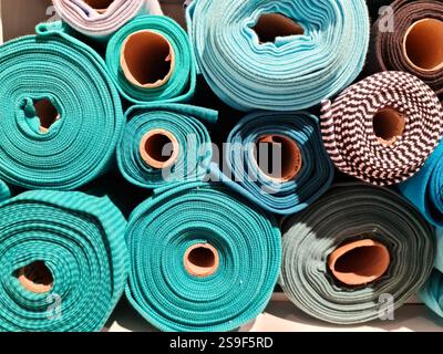 Rolls of colorful ribbed and patterned fabrics are neatly arranged on a shelf, showcasing a variety of textures and colors Stock Photo