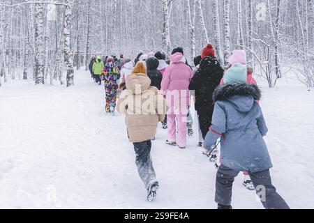 A cheerful group of children in colorful winter clothing walking together through a snowy forest pathway, A group of children on a walk through the wi Stock Photo