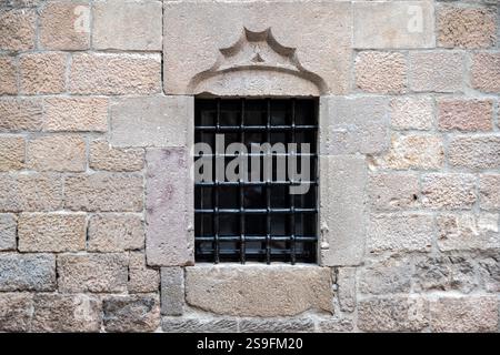Rectangular window with black cast iron grille on old beige stone wall. From the series Windows of the World. Stock Photo
