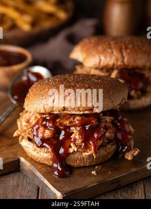 Barbeque pulled chicken sandwichs on whole wheat bun on wooden cutting board with french fries in background Stock Photo