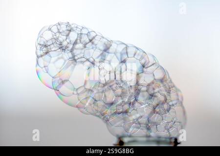 Transparent foam with iridescent bubbles coming out of a plastic bottle with light defocused background Stock Photo