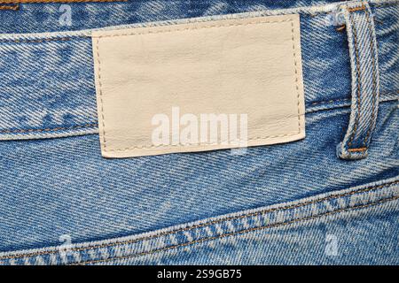 Close-up of blue denim jeans featuring an empty beige leather patch, detailed stitching, and a belt loop, ideal for branding, fashion, or textile Stock Photo