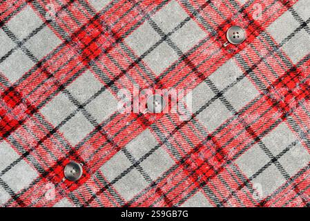 Close up of red and black tartan plaid fabric with gray background, featuring four black buttons. Perfect for fashion, textile, or pattern design Stock Photo