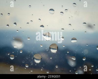 A window with raindrops on it. The raindrops are scattered all over the window, creating a blurry and hazy effect. Scene is calm and peaceful, as the Stock Photo