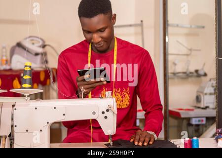 An African tailor using his phone while working in his workshop. Stock Photo