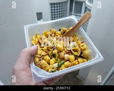 Hand holding a colorful pasta dish with a wooden spoon outside a balcony Stock Photo