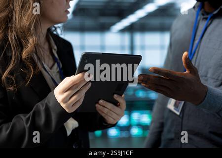 Teamworking employees in data center facility use tablet, configuring rigs network virtualization. IT professional and colleague in server farm updating storage arrays with device, verifying settings Stock Photo