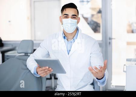 Portrait of handsome arab dentist in medical mask using digital tablet Stock Photo