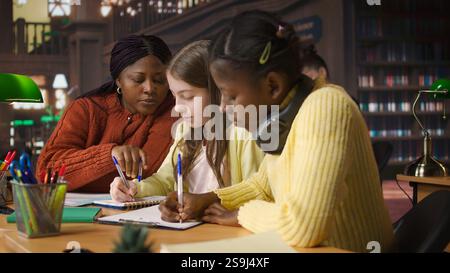 Female teacher assisting pupils with class homework and mentoring, providing academic instruction and support to help pass school assignments. Tutor lecturer gives private lessons. Camera A. Stock Photo
