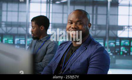 Portrait of happy server room worker developing disaster recovery plans ensuring minimal downtime. Smiling technician in data center using data analytics to monitor performance, camera A Stock Photo