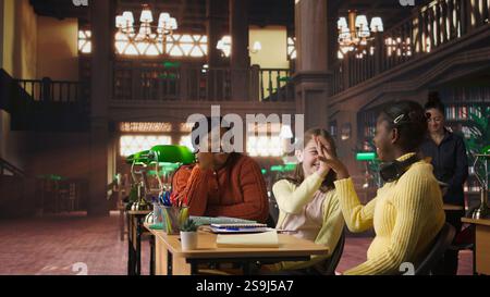 African american teacher providing instruction to diverse girls during private sessions, assisting with homework and school projects in a library. Doing tutoring activity for success. Camera A. Stock Photo