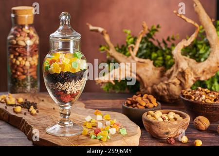 Mix of Nuts and Dry Fruits in a Beautiful Glass Vase. Tree Branch on a Background. Walnuts, Peanuts, Pecan, Almonds, Cashews, Pistachio, Apricot, Rais Stock Photo