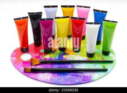 Colorful tubes of paint on a palette with brushes, isolated on white background. Stock Photo