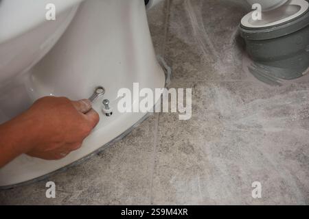 Plumber installs toilet on silicone sealant and bolts it in place Stock Photo