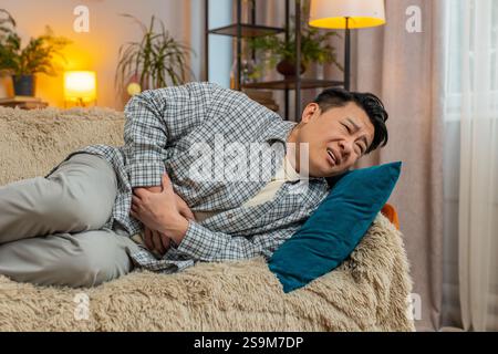 Mature ill sick man lying on sofa feeling sudden strong abdominal stomach ache, gastritis problem. Middle-aged guy having symptom poisoning diarrhea indigestion peptic ulcer pancreatitis at home. Stock Photo