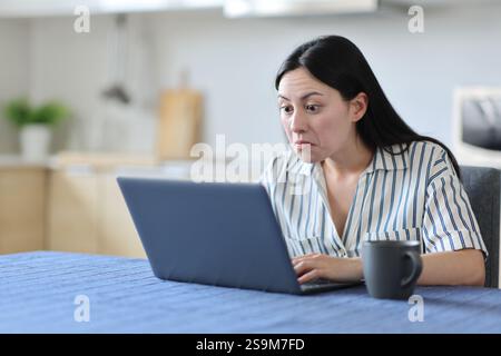Perplexed asian woman using laptiop in the kitchen at home Stock Photo