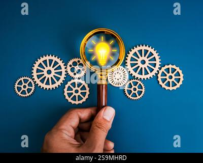 Creative idea and inspiration searching tools, AI solution management workflow concept. Yellow lightbulb icon in magnifying glass lens in human hand w Stock Photo