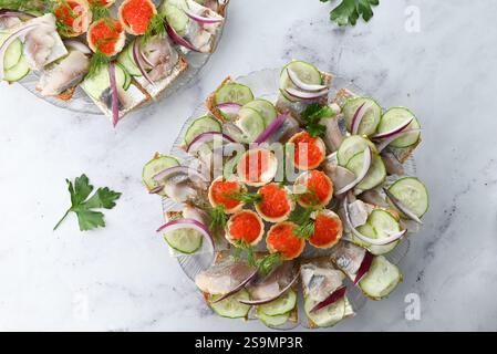 Open-faced sandwiches with various toppings like cucumber, onion, fish, and caviar on a white plate. Made with different bread types, garnished with d Stock Photo