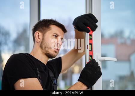 Professional builder using red spirit level for alignment of window frame during installation. Repairman adjusting white pvc windows. Concept of repai Stock Photo
