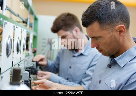 two male technicians working on electrical panel with dials Stock Photo