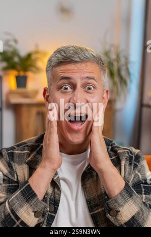 Oh my God, Wow. Young Caucasian man surprised looking at camera with big eyes, shocked by sudden victory, good win news, celebrating. Portrait of excited amazed guy at home apartment room on sofa. Stock Photo