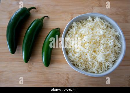 Three green jalapenos, bowl shredded cheese, wood board. Stock Photo