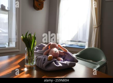 Tulips vase with pink stuffed bunny toy and highchair in kitchen nook Stock Photo