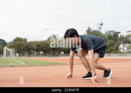 Determined young man preparing to sprint on a track, focused on his fitness and athletic training Stock Photo
