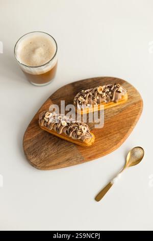 Overhead view eclairs on wooden tray coffee cup spoon on white table Stock Photo