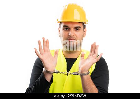 Builder man wearing protective hardhat and vest with sad expression showing handcuffs arrested as corruption concept isolated on white background Stock Photo