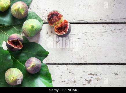 Fresh ripe organic figs with green leaves on white wooden background, healthy summer fruit, Ficus carica ( Moraceae ) Stock Photo