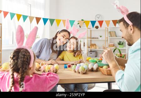 Happy family with children wearing bunny ears painting Easter eggs and preparing for celebration. Stock Photo