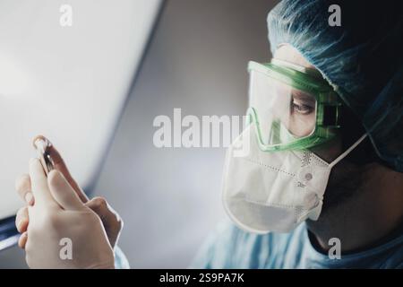 A doctor in green goggles examines a vial while wearing a mask Stock Photo